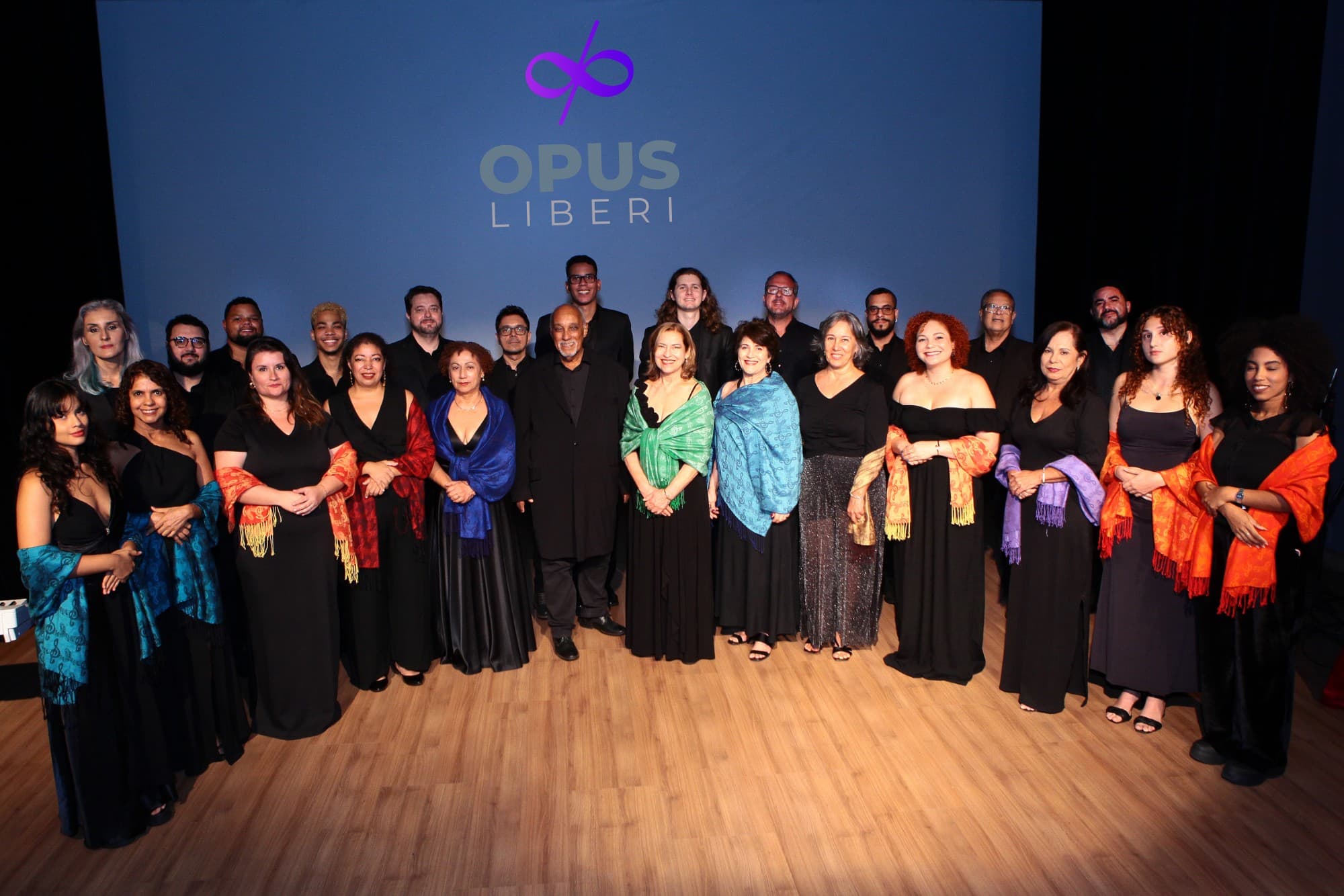 Coral Opus Liberi posando no palco, com a marca do coral projetada ao fundo