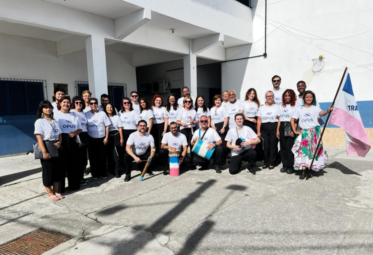 Coralistas do Opus Liberi reunidos ao ar livre, de camiseta do coral, com tambores e bandeira